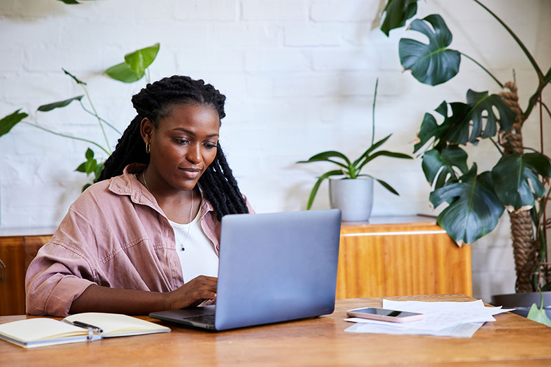 Focused young woman working remotely from home on a laptop - stock photo